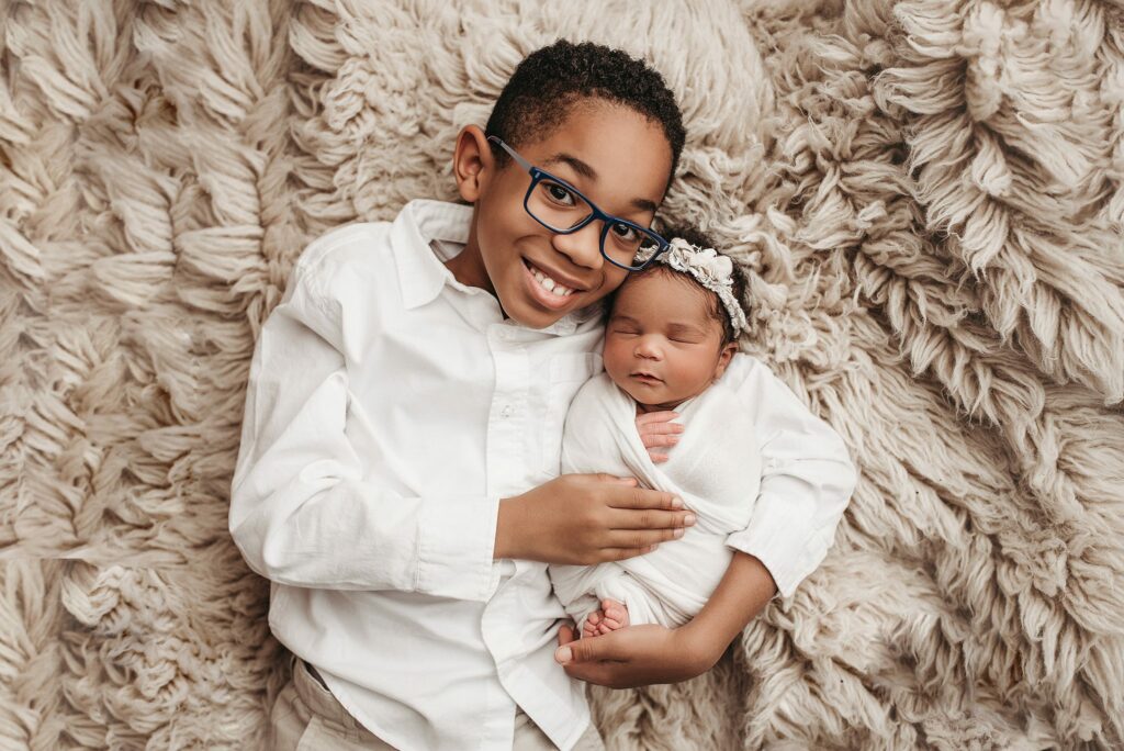 big brother holding baby sister for her newborn photography session in atlanta, ga, neutral colored newborn session set ups, newborn girl sleeping with big brother, sibling poses for newborn photography session, atlanta baby photography, newborn photographer in atlanta