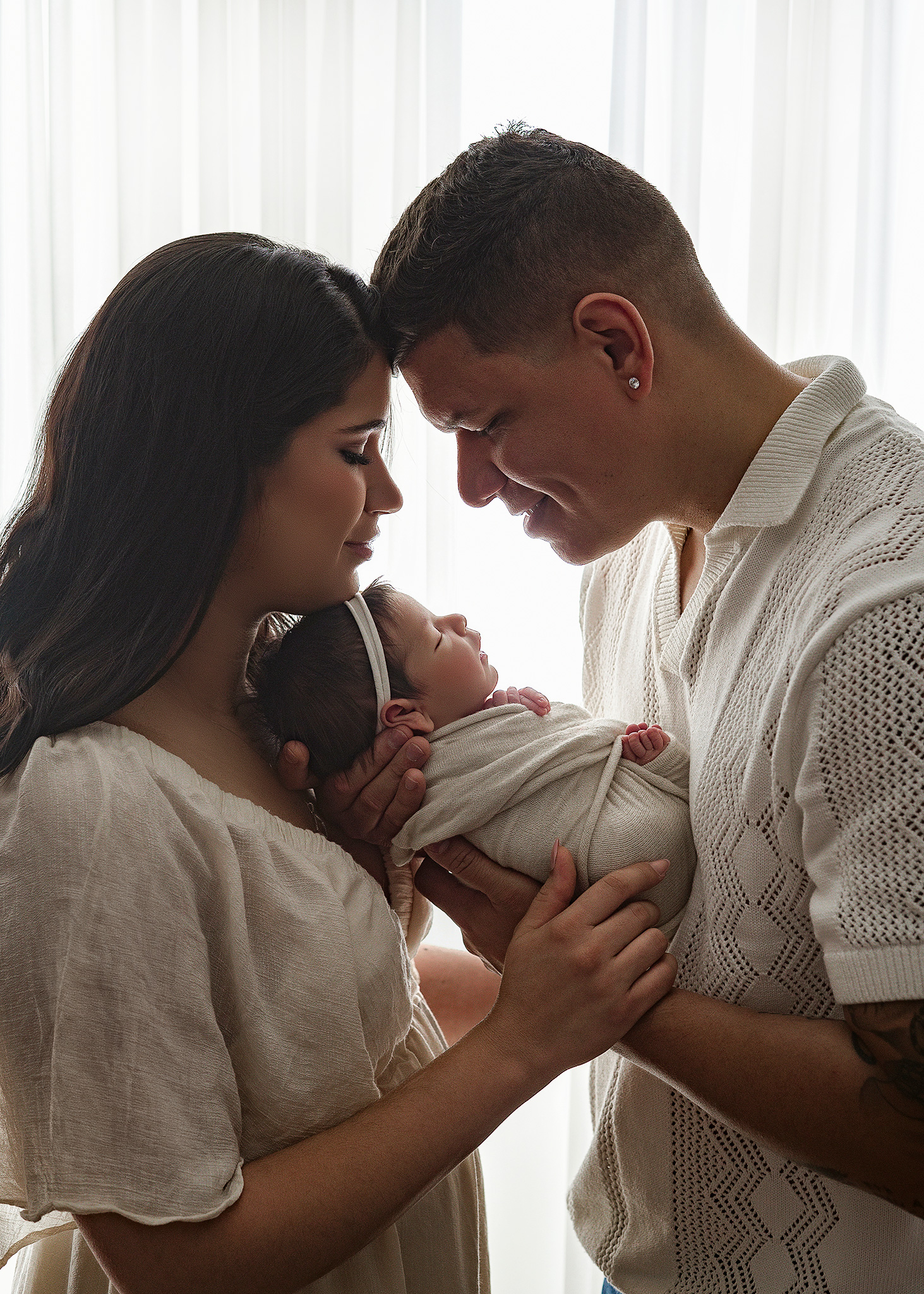 mom and dad resting heads during newborn photoshoot, baby girl swaddled in white for photo session in lincoln portrait studio