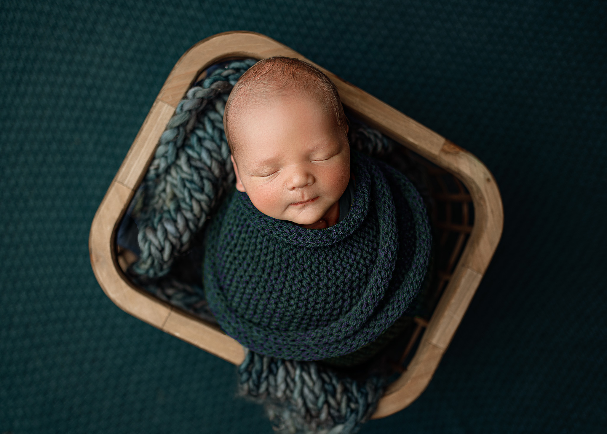 newborn photographer in lincoln photographs baby boy in a teal wrap with a monochromatic look